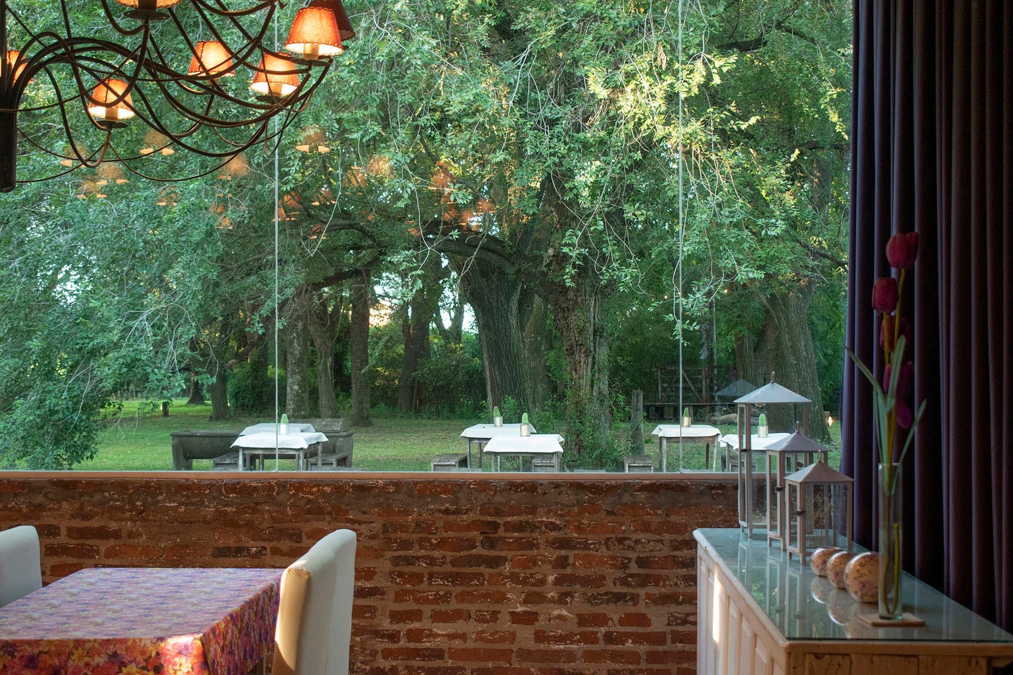 Mesa junto al ventanal del comedor, con el parque iluminado del otro lado del vidrio.