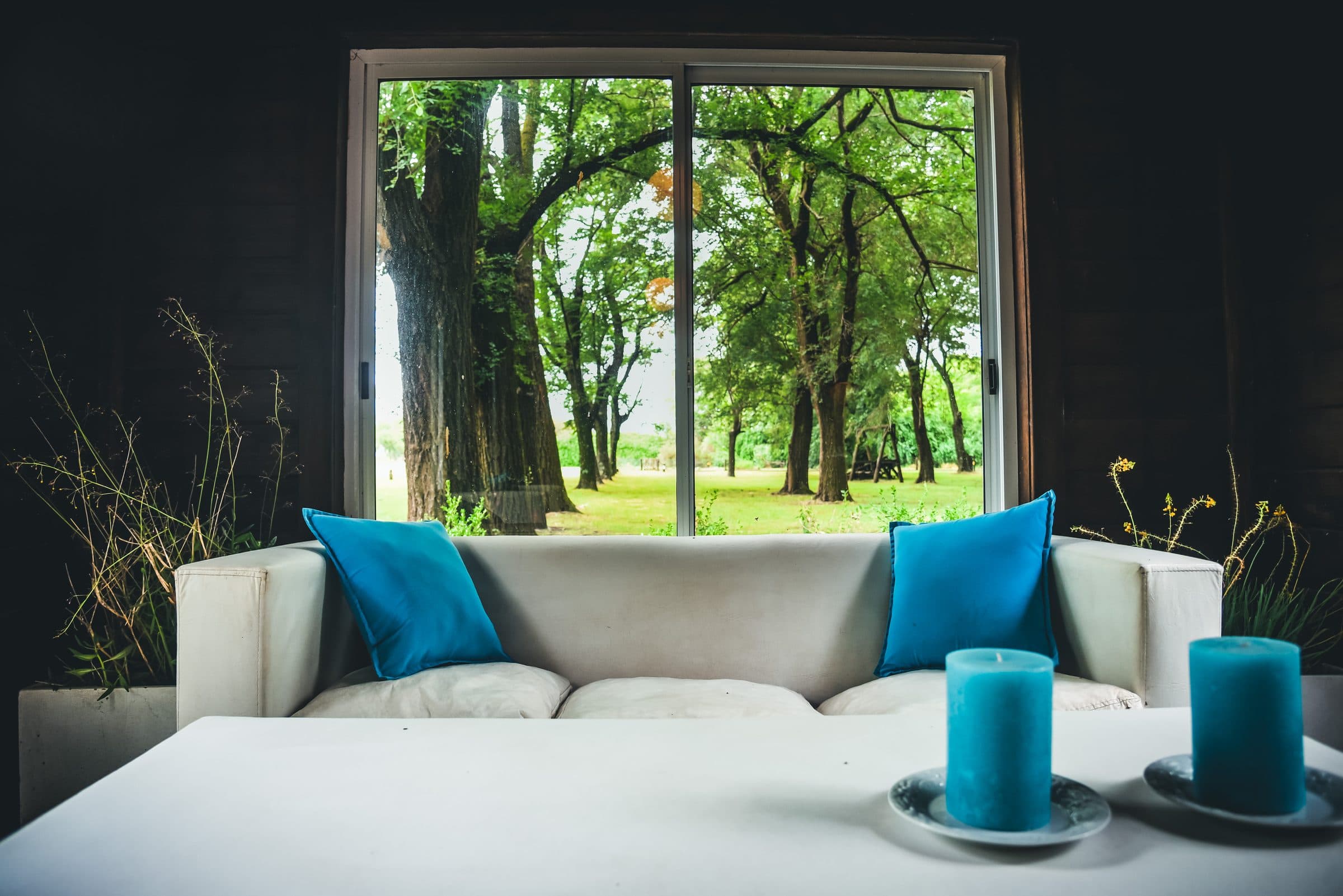 Estar del spa: un sillón blanco con almohadones turquesa frente al ventanal que da a la arboleda, con velas y ramas secas sobre la mesa baja.